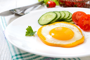 Fried egg in a circle of sweet pepper on a white plate with fresh vegetables on a white wooden background. Delicious healthy breakfast. Proper nutrition.