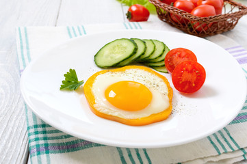 Fried egg in a circle of sweet pepper on a white plate with fresh vegetables on a white wooden background. Delicious healthy breakfast. Proper nutrition.