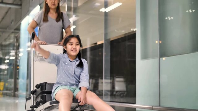 4K Happy Asian girl sitting on luggage trolley in the airport, play with mother while waiting for the flight