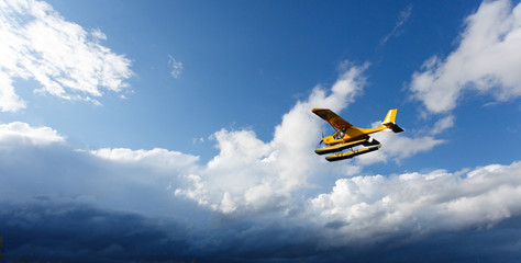 A small yellow hydroplane flying in sky