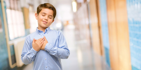 Handsome toddler child with green eyes with hands in heart, expressing love and health concept at school corridor