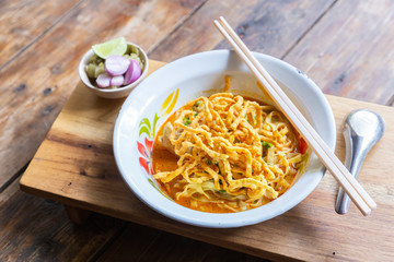 Curried noodle soup (Khao soi) with chicken meat and spicy coconut milk on wood table. Thai food cuisine northern style in Chiang Mai.
