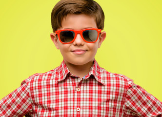 Handsome toddler child with green eyes confident and happy with a big natural smile laughing over yellow background