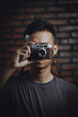 Asian Man Taking Picture With Vintage Camera on Brick Wall Background