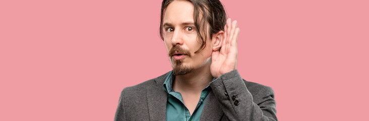 Handsome young man holding hand near ear trying to listen to interesting news expressing...