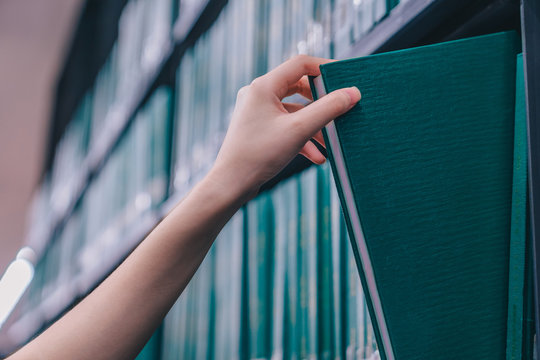 Hand pulling a Thesis book off the shelf in Library. Green colors books.