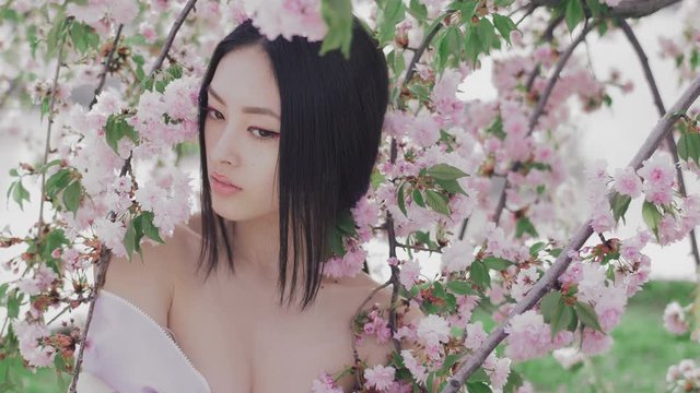 Backstage of outdoor photoshoot of beautiful young asian woman surrounded by flowers on spring. Perfect model with creative vivid makeup and pink lipstick on lips and traditional japanese hairstyle