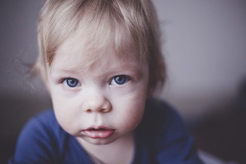 Cute little blond kid with blue eyes in blue clothes looking right into the camera. Close up. Imitation of film grain.