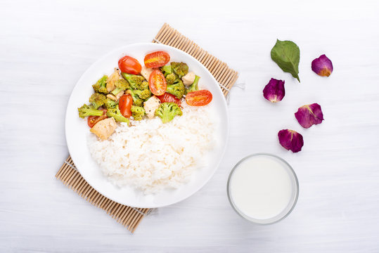 Fried broccoli with tomatoes,chicken and cooked rice on white dish and glass of milk,Asian cuisine, top view