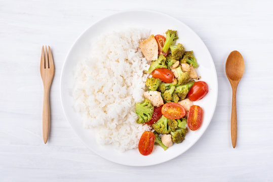 Fried broccoli with tomatoes, chicken and cooked rice on white dish, Asian cuisine, top view