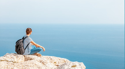 Fototapeta na wymiar A girl traveler sits on a rock and admires the blue boundless sea, freedom, travel, unity with nature