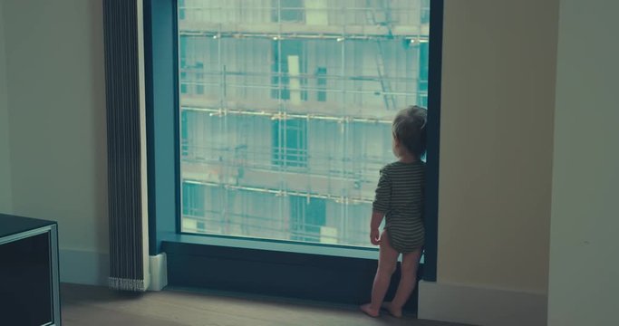 Little boy standing by window in city apartment