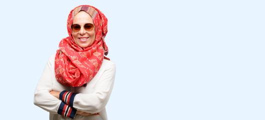 Middle age muslim arab woman wearing hijab with crossed arms confident and happy with a big natural smile laughing isolated blue background