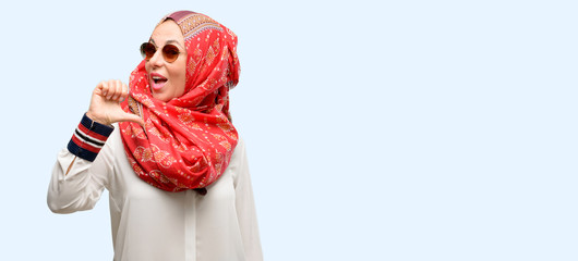 Middle age muslim arab woman wearing hijab proud, excited and arrogant, pointing with victory face isolated blue background