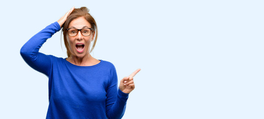 Middle age woman wearing wool sweater and glasses pointing away side with finger isolated blue background