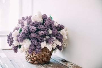 Bouquet of white and purple lilac flowers in wicker basket on ta