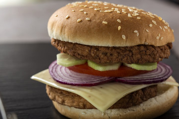Close up of a cheeseburger with tomato, onion and cucumber