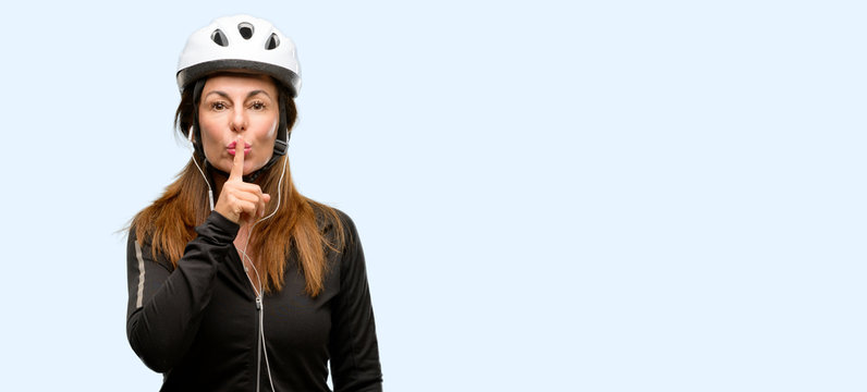 Middle Age Cyclist Woman Using Earphones With Index Finger On Lips, Ask To Be Quiet. Silence And Secret Concept Isolated Blue Background