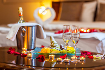 Hotel room for a honeymoon: a table with a fruit plate and candles, in the background a bed decorated with swans of towels and rose petals