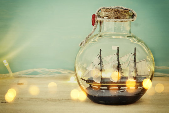 nautical concept image with sail boat in the bottle and gold garland lights over wooden table. Selective focus.