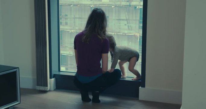 Mother by the window in the city picks up toddler
