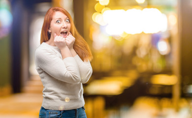 Beautiful young redhead woman happy and surprised cheering expressing wow gesture at night