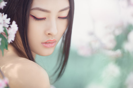 Gorgeous fantasy girl face dreaming with closed eyes against nature beauty background. Perfect model with creative vivid makeup and pink lipstick on lips and traditional japanese hairstyle posing