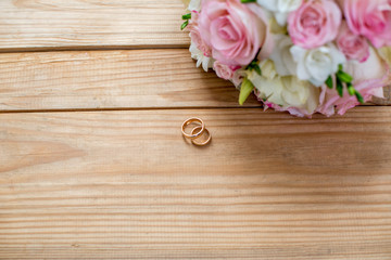 Two gold wedding rings and beautiful wedding are on the brown wood table