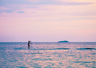 standup paddler auf dem Meer in der Dämmerung mit einer kleinen Insel