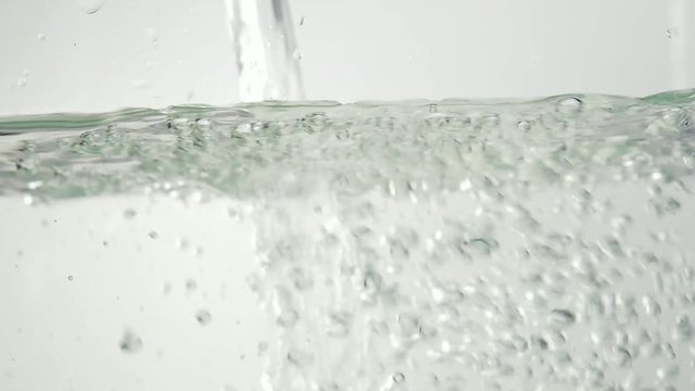 Water pouring on surface and splashing. Bubbles rising in water on white background. Shooting of pouring water closeup. Shot at 60fps HD format.