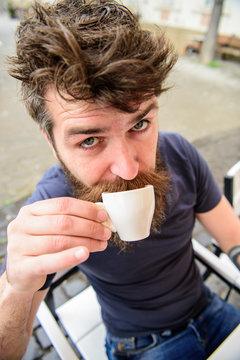 Hipster on surprised face drinking coffee outdoor. Man with beard and mustache holds cup of coffee while relaxing at cafe terrace. Coffee break concept. Guy having rest with espresso coffee.