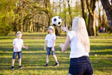 Obraz premium Mother playing with ball with her sons on green grass in park.