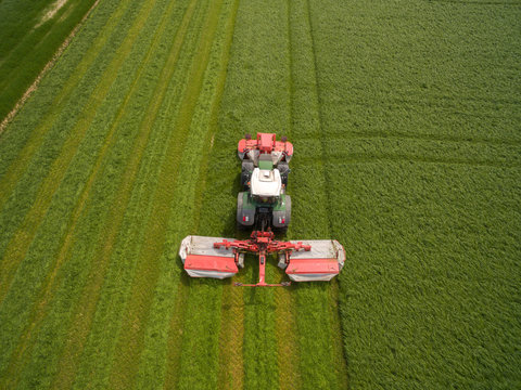 
Aerial view of a tractor mowing a green fresh grass field, 
a farmer in a modern tractor mowing a green fresh grass field on a sunny day