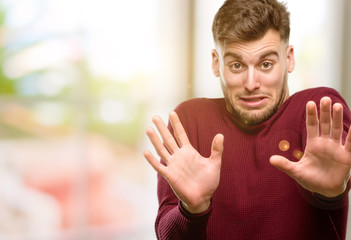 Handsome young man disgusted and angry, keeping hands in stop gesture, as a defense, shouting