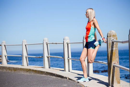 Beautiful blond female fitness athlete stretching before her outdoor run next to the ocean
