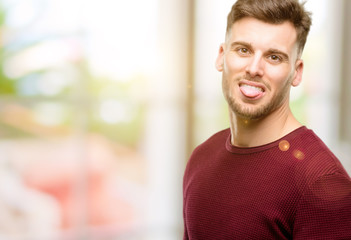 Handsome young man sticking out tongue at camera at sign of disobedience, protest and disrespect