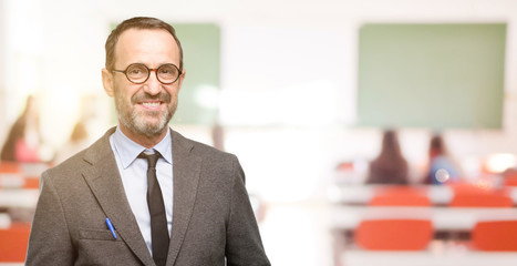 Teacher man using glasses confident and happy with a big natural smile laughing at classroom