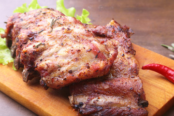 grilled barbecued ribs with lettuce leaves, hot chili pepper and sauce on wooden cutting board.