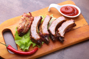 grilled barbecued ribs with lettuce leaves, hot chili pepper and sauce on wooden cutting board.