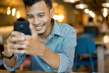 close up asian man using smartphone with happy feeling at coffee cafe shop concept