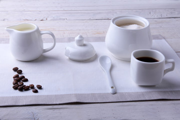 Cup of hot coffee espresso, coffee beans, jug of milk, and bowl with sugar on white background for copy space. Coffee concept.