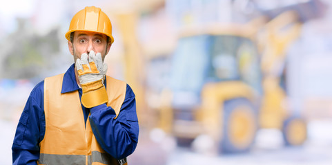 Senior engineer man, construction worker covers mouth in shock, looks shy, expressing silence and...