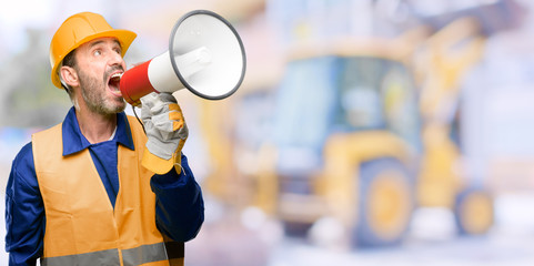 Senior engineer man, construction worker communicates shouting loud holding a megaphone, expressing...