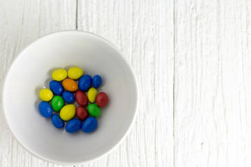 Colorful candy in a bowl on a wooden white painted table