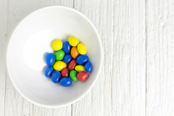 Colorful candy in a bowl on a wooden white painted table