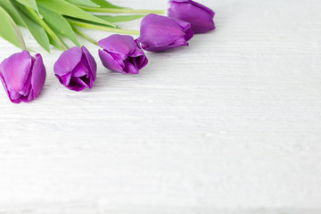 A bunch of purple tulips on a white wooden table.