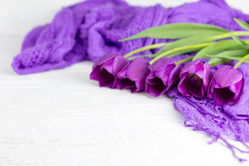 A bouquet of purple tulips and a purple cloth on a white wooden table.