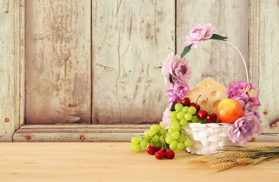 image of fruits and cheese in decorative basket with flowers over wooden table. Symbols of jewish holiday - Shavuot.