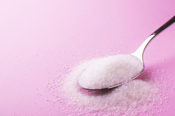 spoon with sugar on a pink background, side view