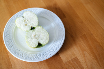 Two halves of a green apple are sprinkled with sugar on a plate and on a wooden table, minimalism.